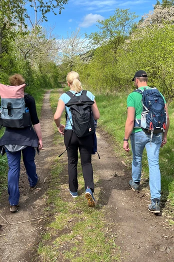 Wandern in der Mittelweser-Region Drei Personen wandern auf einem naturbelassenen Weg, umgeben von frischem Grün und blauem Himmel.