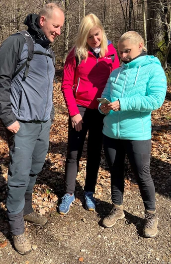 Three people stand on an autumnal forest path and look at a smartphone together.