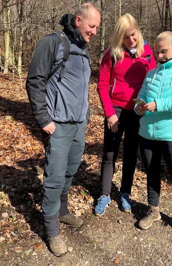 Wandern in der Mittelweser-Region Drei Menschen stehen auf einem herbstlichen Waldweg und betrachten gemeinsam ein Smartphone.