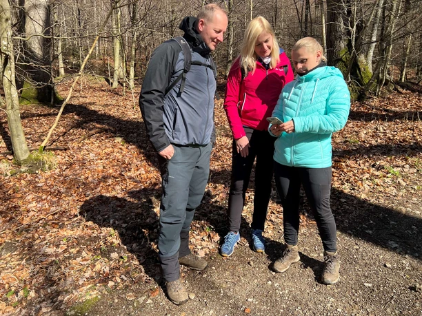 Wandern in der Mittelweser-Region Drei Menschen stehen auf einem herbstlichen Waldweg und betrachten gemeinsam ein Smartphone.