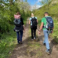 Wandern in der Mittelweser-Region Drei Wanderer auf einem naturbelassenen Pfad, umgeben von grüner Vegetation und blauem Himmel.