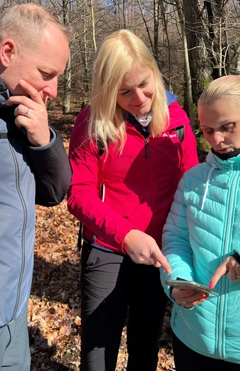 Gruppe wandernd im lichten Laubwald, fokussiert auf ein Smartphone als Wanderhilfe im herbstlichen Umfeld.