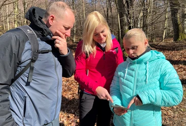 Group hiking in a sparse deciduous forest, focused on a smartphone as a hiking aid in the autumnal surroundings.