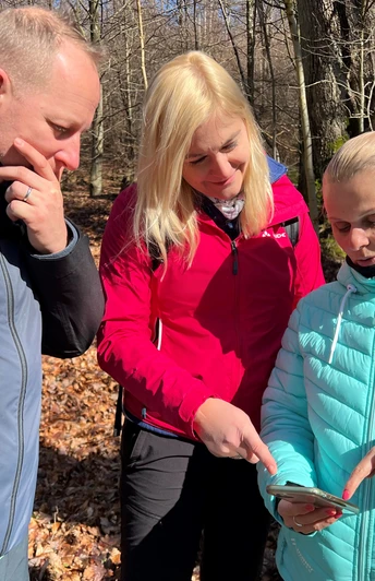 Groepswandeling in een schaars loofbos, gericht op een smartphone als wandelhulp in de herfstachtige omgeving.