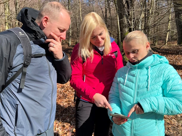Groepswandeling in een schaars loofbos, gericht op een smartphone als wandelhulp in de herfstachtige omgeving.