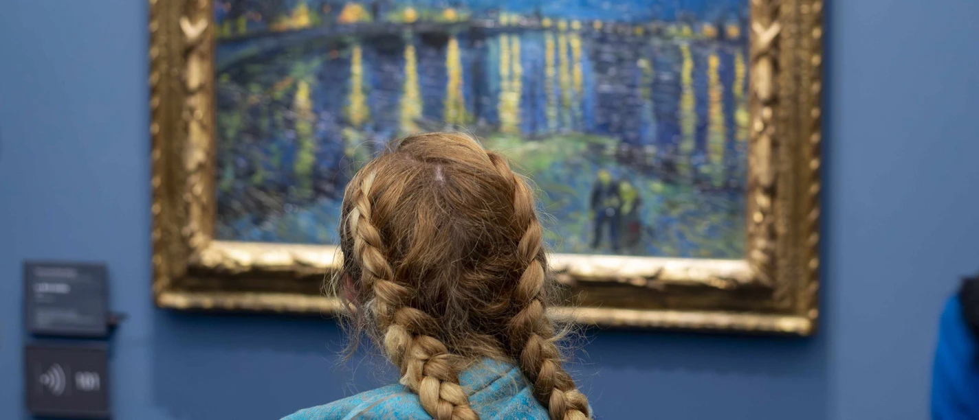 11 Sekunden_Van Gogh (c) Stefan Draschan.jpg Ein Mädchen mit blonden Haaren und einem geflochtenen Zopf steht vor einem blauen Van Gogh Gemälde mir Sternenhimmel.