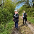 Zwei Wanderinnen mit Rucksäcken auf einem Pfad durch eine grüne, dichte Waldlandschaft.