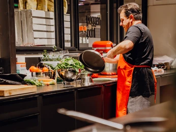 MarkthalleHerford-16.jpg Ein Mann in roter Schürze bereitet mit einem Standmixer und frischen Zutaten Essen zu.