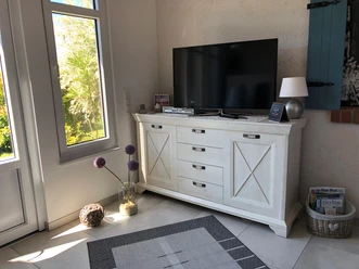 Zwetschenbrummer Ein freundlich wirkendes Wohnzimmer mit einer hellen Kommode und einem großen Flachbildfernseher.