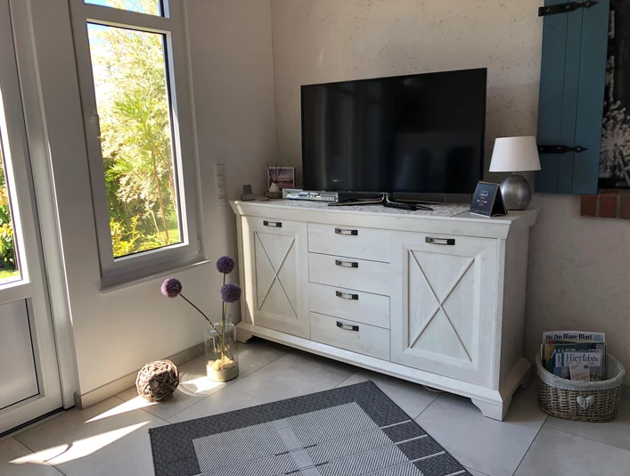 Zwetschenbrummer Ein freundlich wirkendes Wohnzimmer mit einer hellen Kommode und einem großen Flachbildfernseher.
