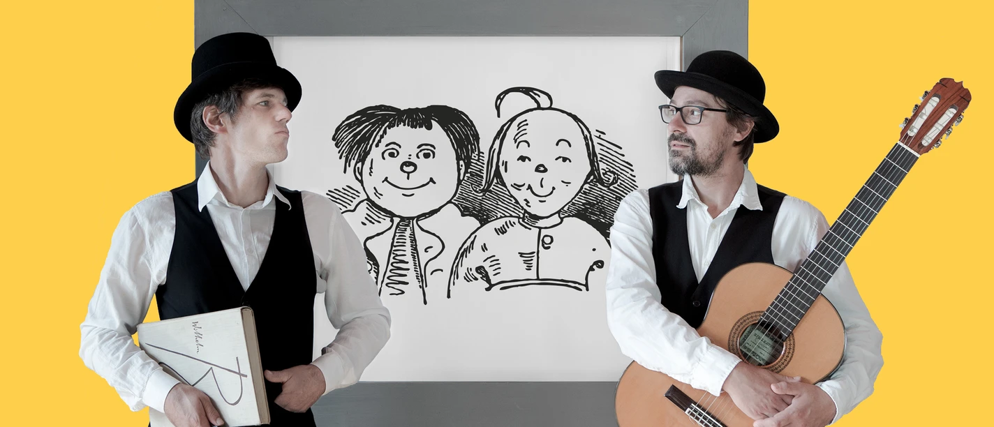 251026_Kids_Kurbeltheater.jpg Zwei Männer in schwarzen Westen und Hüten stehen lächelnd vor einer Zeichnung, einer spielt Gitarre.