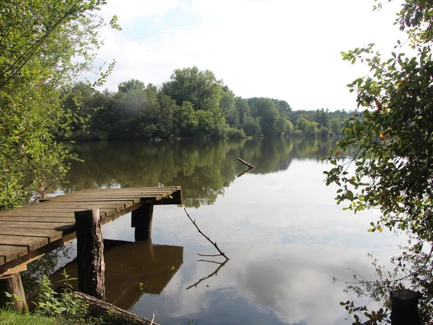 POI_0_Hücker Moor.JPG Holzsteg am Ufer eines ruhigen Sees, umgeben von üppigem Grün und Bäumen. Friedliche Atmosphäre.