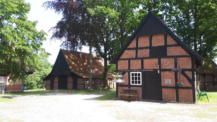 Heimathof Emsbüren – Backhaus ©Emsland Tourismus GmbH (1).jpg Backhaus mit rotem Fachwerk und dunklen Balken auf dem Heimathof Emsbüren, umgeben von Bäumen.