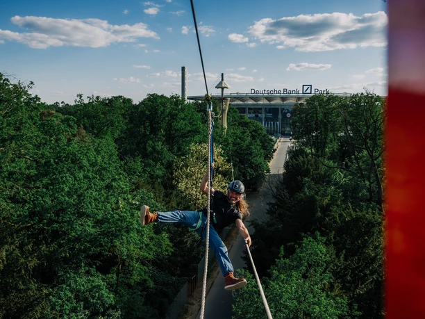 Kletterwald Kletterer an Seilrutsche mit Blick auf Stadion und Baumwipfel