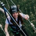 Kletterwald Junge Frau im Klettergurt lächelt beim Aufstieg im Parcours