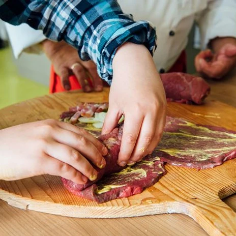 k-blankenhain-rouladen-machen-5-c-tmgs-czech-vibes.jpg Zwei Hände bereiten Rouladen aus rohem Fleisch und Senf auf einem hölzernen Brett zu.