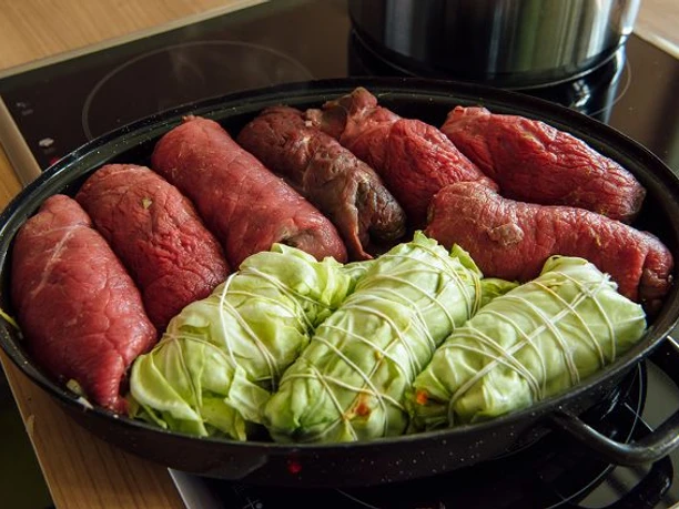 k-blankenhain-rouladen-machen-7-c-tmgs-czech-vibes.jpg Rinderrouladen und Kohlrouladen auf einem Herd in einem schwarzen Bräter.