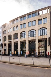 Das Bild zeigt die Fassade des Kölnischen Stadtmuseums, ein modernes Gebäude mit großen Fenstern und hellen Steinwänden. Der Eingang ist zur Straße hin ausgerichtet, flankiert von Informationsschildern und Plakaten, die auf aktuelle Ausstellungen hinweisen.