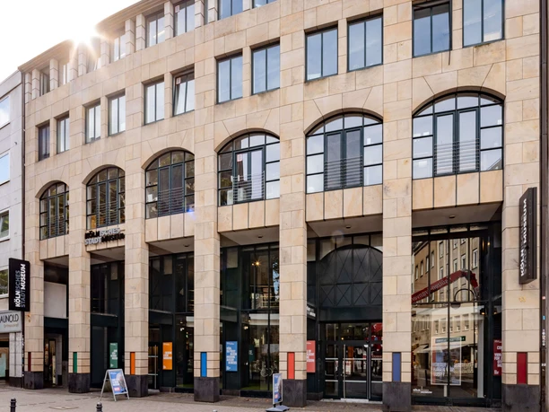 Kölnisches Stadtmuseum Das Bild zeigt die Fassade des Kölnischen Stadtmuseums, ein modernes Gebäude mit großen Fenstern und hellen Steinwänden. Der Eingang ist zur Straße hin ausgerichtet, flankiert von Informationsschildern und Plakaten, die auf aktuelle Ausstellungen hinweisen.