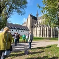 LuGeV-Führung in Altenberg Gruppe von Menschen steht vor einer historischen Kirche aus Stein an einem sonnigen Tag, umgeben von Bäumen.