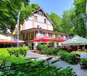 Biergarten in der Schlesischen Schänke im Engelsberger Hof Biergarten der Schlesischen Schänke in Solingen, umgeben von Bäumen, mit bunten Schirmen und Sitzflächen.