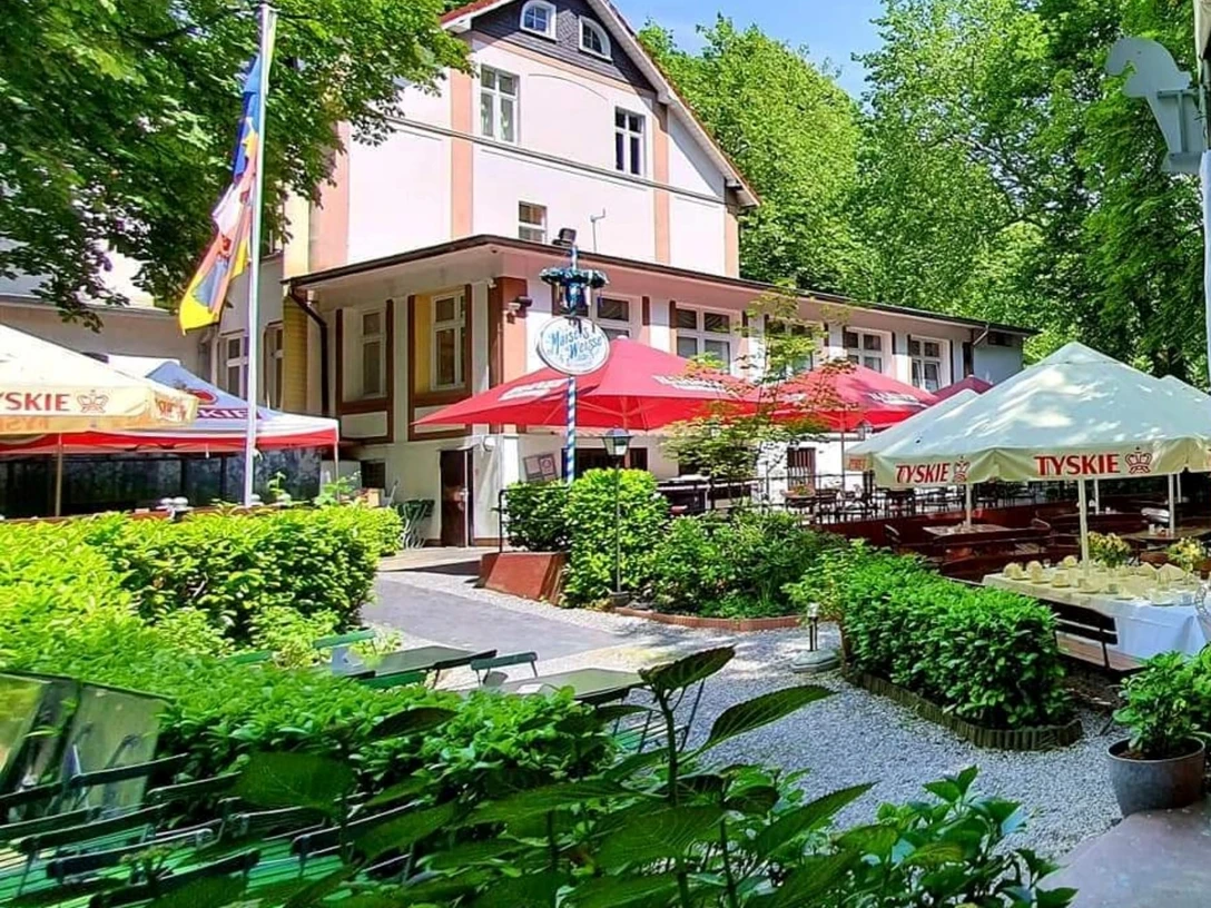 Biergarten in der Schlesischen Schänke im Engelsberger Hof Biergarten der Schlesischen Schänke in Solingen, umgeben von Bäumen, mit bunten Schirmen und Sitzflächen.