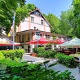 Biergarten in der Schlesischen Schänke im Engelsberger Hof Biergarten der Schlesischen Schänke in Solingen, umgeben von Bäumen, mit bunten Schirmen und Sitzflächen.