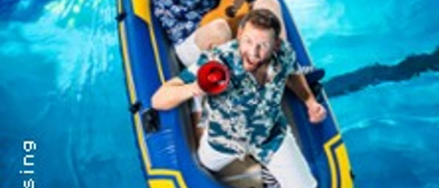 Zwei lachende Personen in Hawaii-Hemden treiben in einem Schlauchboot auf klarem, blauem Wasser.