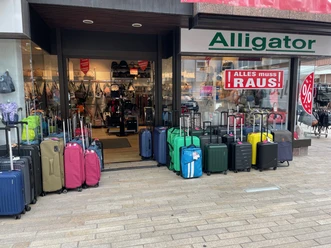 Schaufenster und Eingangsbereich des Geschäfts. Neben der Eingangstür stehen jeweils rechts und links Koffer in verschiedenen Farben und Formen.