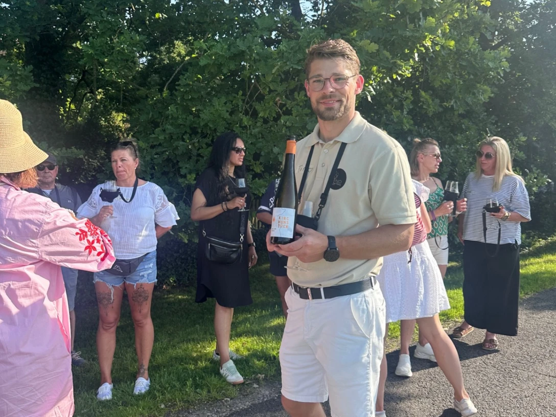 Weinwandern Timo Strauss mit einer Weinflasche in der Hand steht vor einer Gruppe Menschen mit Weingläsern in der Hand