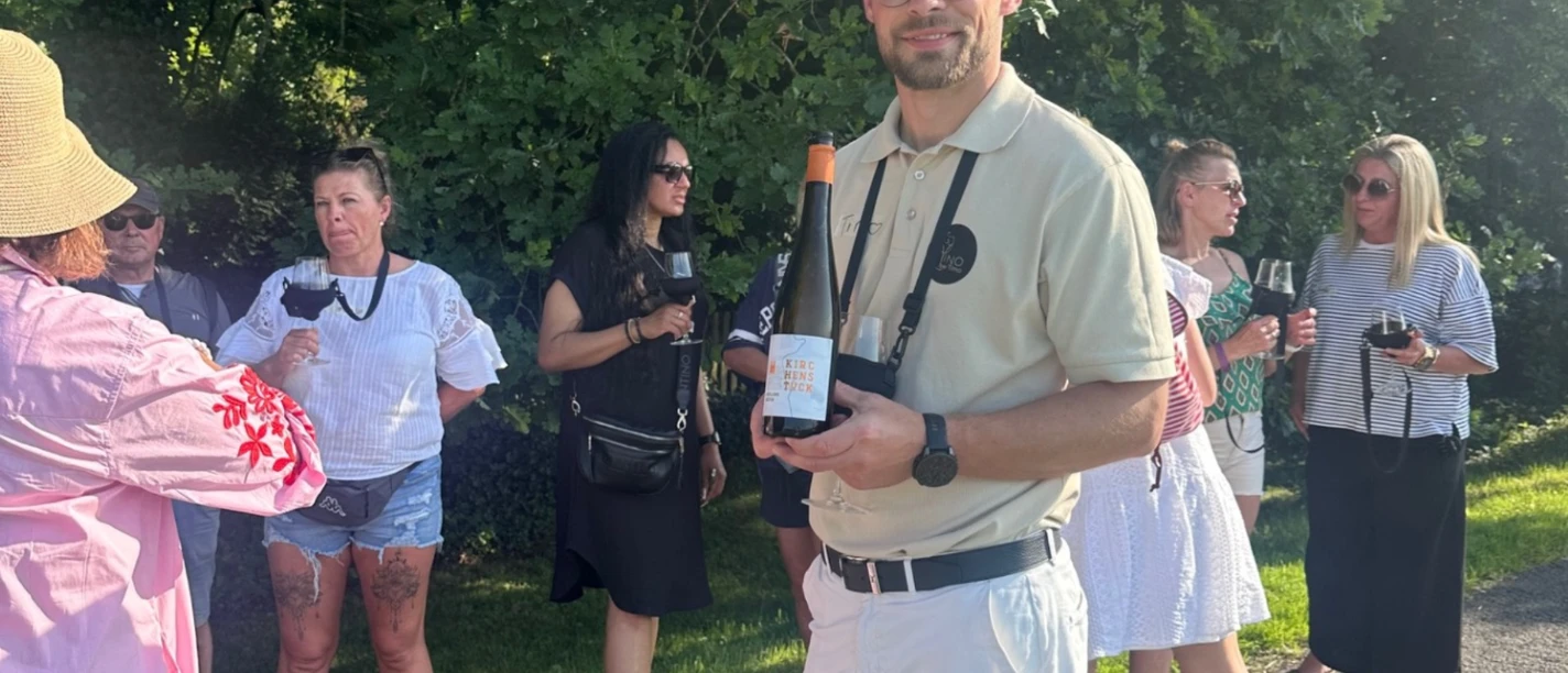 Weinwandern Timo Strauss mit einer Weinflasche in der Hand steht vor einer Gruppe Menschen mit Weingläsern in der Hand