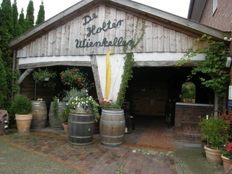 De Holter Wienkeller Eingang zum De Holter Wienkeller mit Holzfass-Dekoration und Pflanzen in Töpfen