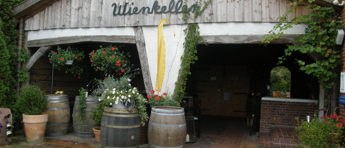 De Holter Wienkeller Eingang zum De Holter Wienkeller mit Holzfass-Dekoration und Pflanzen in Töpfen