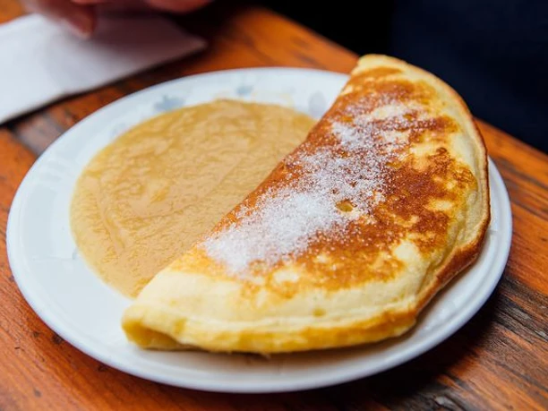 k-schwarzkollm-krabat-muehle-32-c-tmgs-czech-vibes.jpg Ein halbmondförmiger Pfannkuchen auf einem Teller, daneben ein Püree aus Äpfeln.
