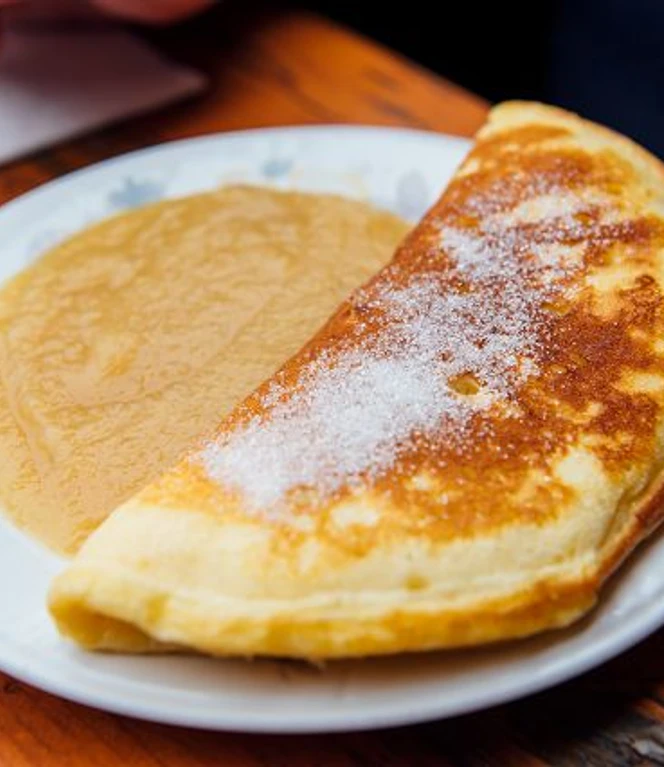 k-schwarzkollm-krabat-muehle-32-c-tmgs-czech-vibes.jpg Ein halbmondförmiger Pfannkuchen auf einem Teller, daneben ein Püree aus Äpfeln.