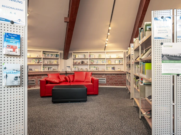 In der Bücherei Seevetal Eine einladende Leseecke mit roten Sofas umrahmt von Bücherregalen in behaglicher Bücherei-Atmosphäre.