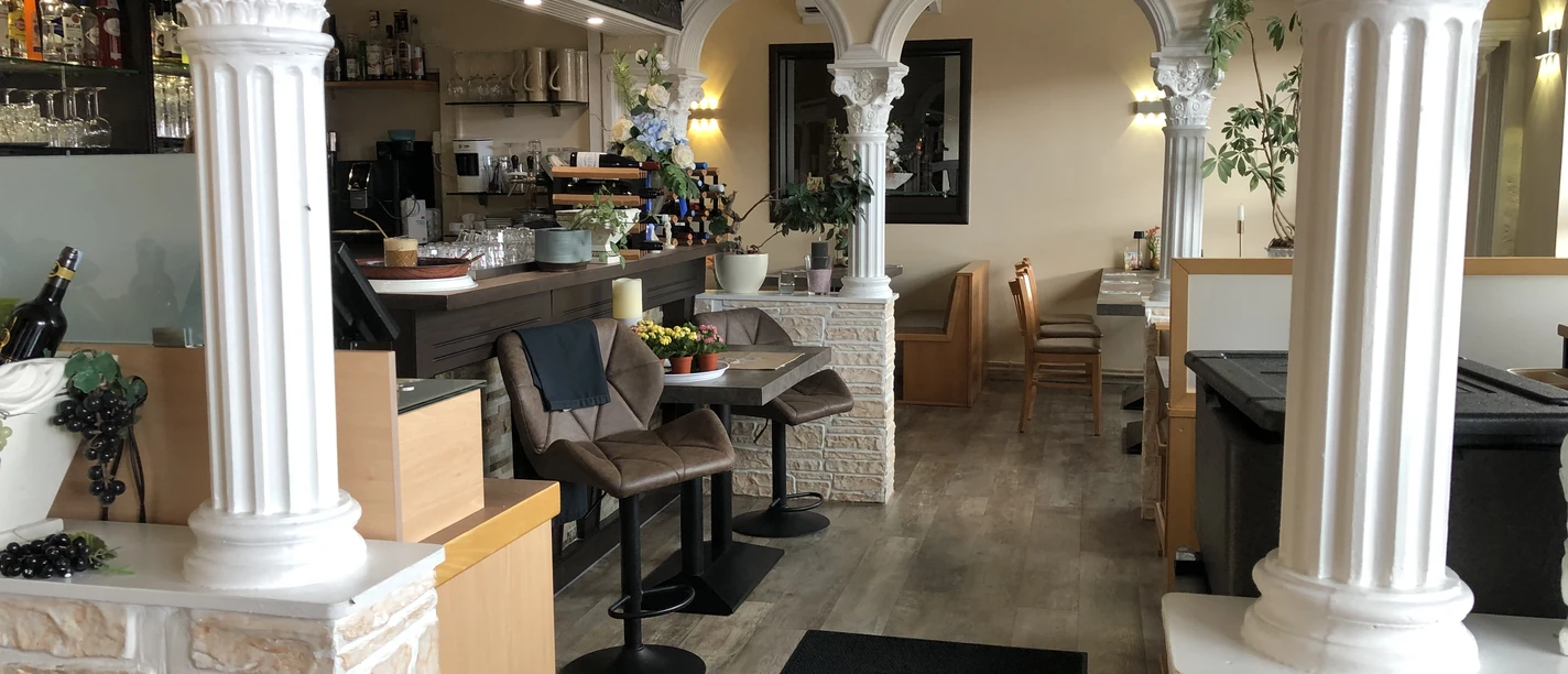 Restaurant mit klassisch-griechischen Säulen und einladender Atmosphäre innen; Bar und Sitzbereiche.