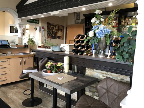 Restaurant Olympia Einladendes Restaurant mit dekorierten Tischen, eleganter Theke und schönem Blumenschmuck im Vordergrund.