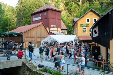Bezoekers genieten van het Kirnitzschtal festival in de open lucht voor de historische Buschmühle midden in de groene natuur.