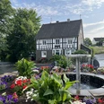 Ortskern Nümbrecht Ein traditionelles Fachwerkhaus mit blühendem Blumenbeet und zentralem Springbrunnen in einer ländlichen Umgebung.