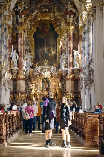 Radpilgern - Wieskirche Innenansicht einer barocken Kirche mit kunstvoll verzierten Wänden und Besuchern.