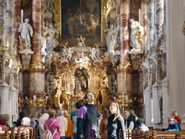 Radpilgern - Wieskirche Innenansicht einer barocken Kirche mit kunstvoll verzierten Wänden und Besuchern.
