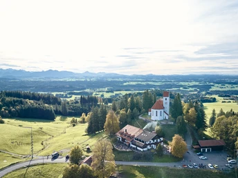 Radpilgern - Auerberg mit Alpenblick Aussicht auf die Alpen und Kirche am Auerberg, von Bäumen und grünen Feldern umgeben.