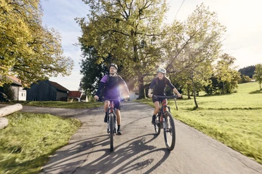 Radpilgern - Auerberg Bernbeuren Zwei Radfahrer auf einem Landweg bei sonnigem Wetter, umgeben von grüner Landschaft.
