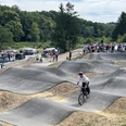 Skate und Bikepark Waldbröl Ein BMX-Fahrer meistert Schwünge auf einer welligen Asphaltstrecke, umgeben von Zuschauern im Freien.