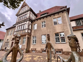 Altes Amtsgericht Petershagen Fachwerkhaus mit roten Ziegeldach und großen Fenstern, davor moderne Skulpturen auf gepflastertem Boden.