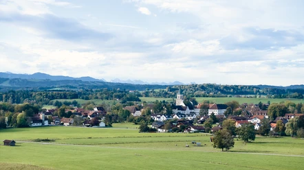 Himmlisch genießen - Polling-Landschaft Weitläufige grüne Landschaft mit Dorf, Kirche und Bergpanorama im Hintergrund.
