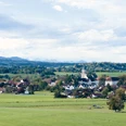 Himmlisch genießen - Polling-Landschaft Weitläufige grüne Landschaft mit Dorf, Kirche und Bergpanorama im Hintergrund.