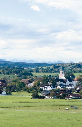 Himmlisch genießen - Polling-Landschaft Weitläufige grüne Landschaft mit Dorf, Kirche und Bergpanorama im Hintergrund.
