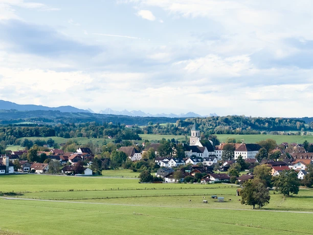 Himmlisch genießen - Polling-Landschaft Weitläufige grüne Landschaft mit Dorf, Kirche und Bergpanorama im Hintergrund.